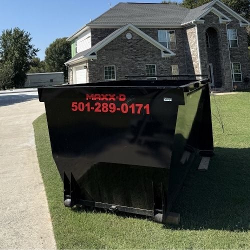 Large black dumpster in front of a two-story suburban brick house
