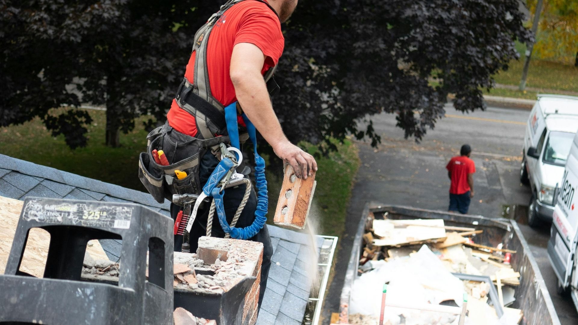Roofer in red shirt working on roof with safety harness and tools