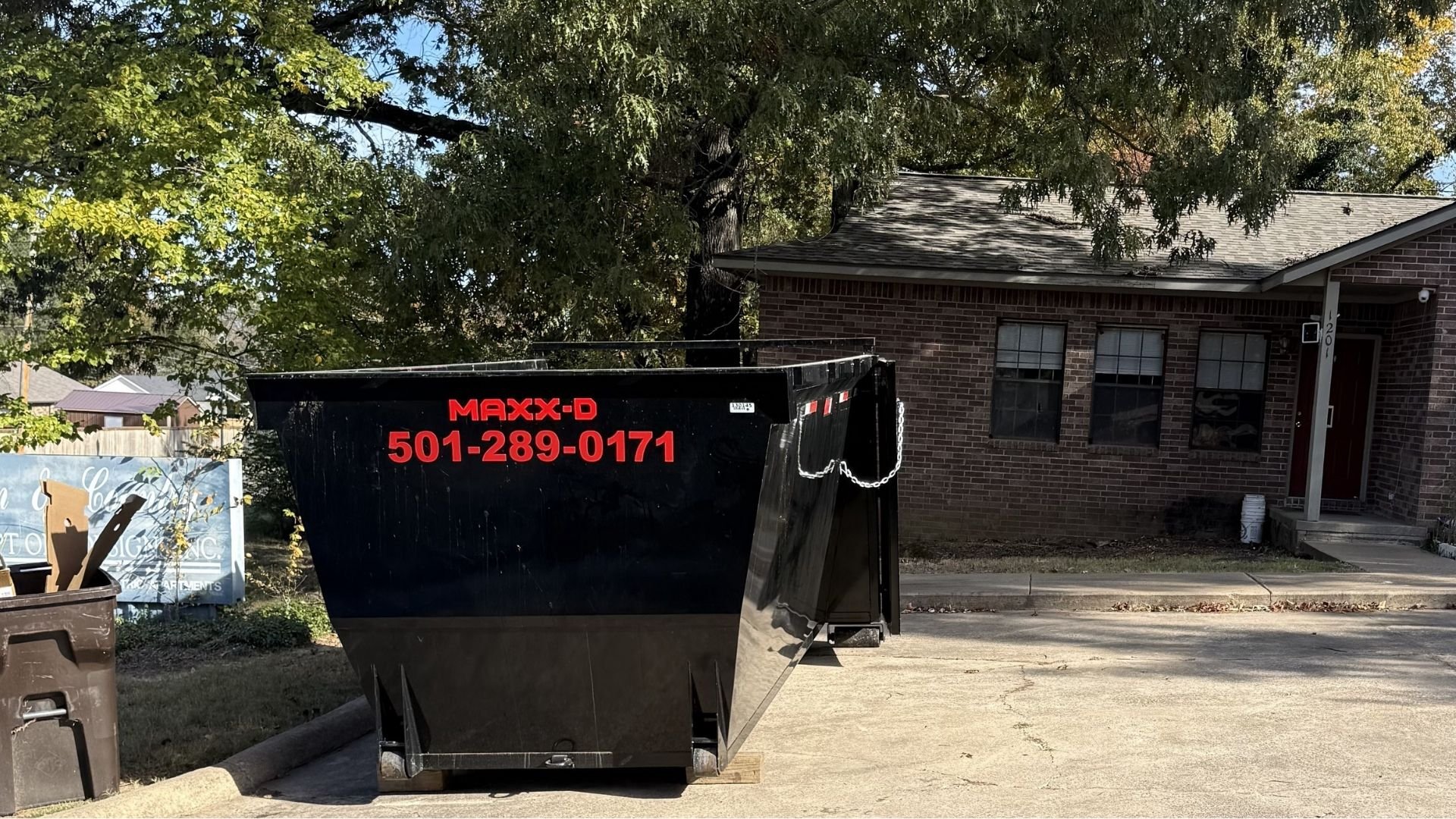 Large black dumpster with Maxx-D logo parked in residential driveway
