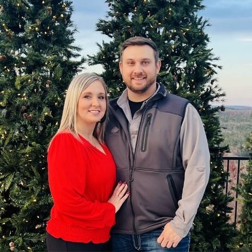 Couple standing together in front of decorated Christmas trees outdoors