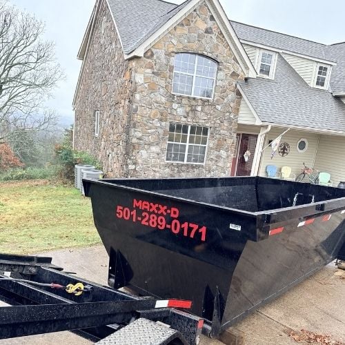 Large black dumpster in driveway of stone and siding suburban house