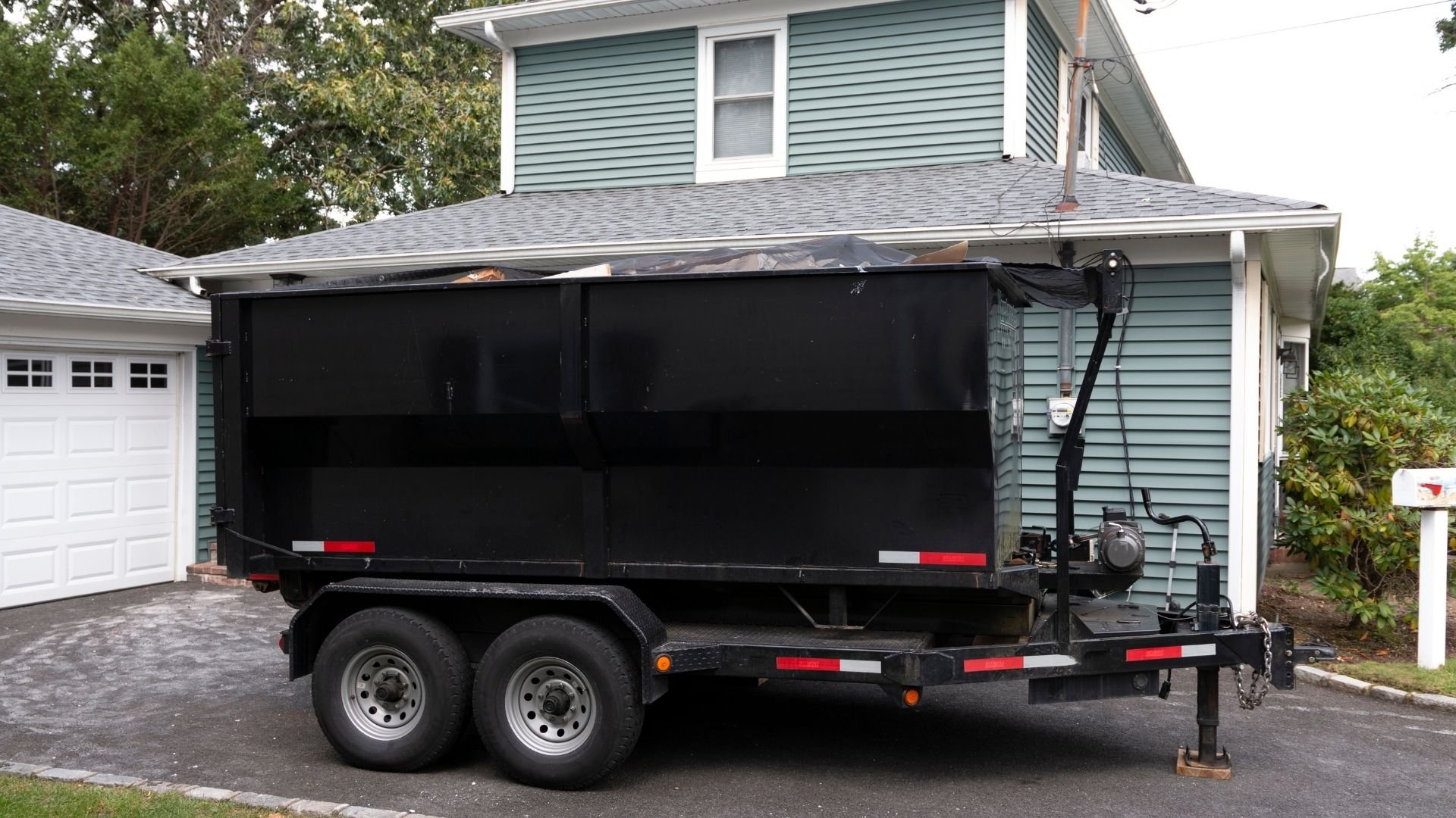 Black two-wheeled dumpster trailer parked in residential driveway