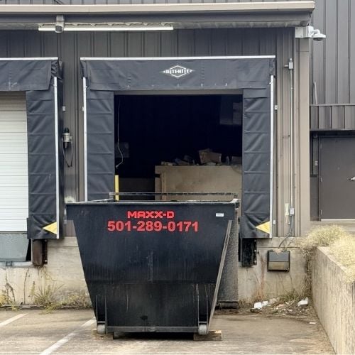 Large black dumpster in front of a loading dock at an industrial building