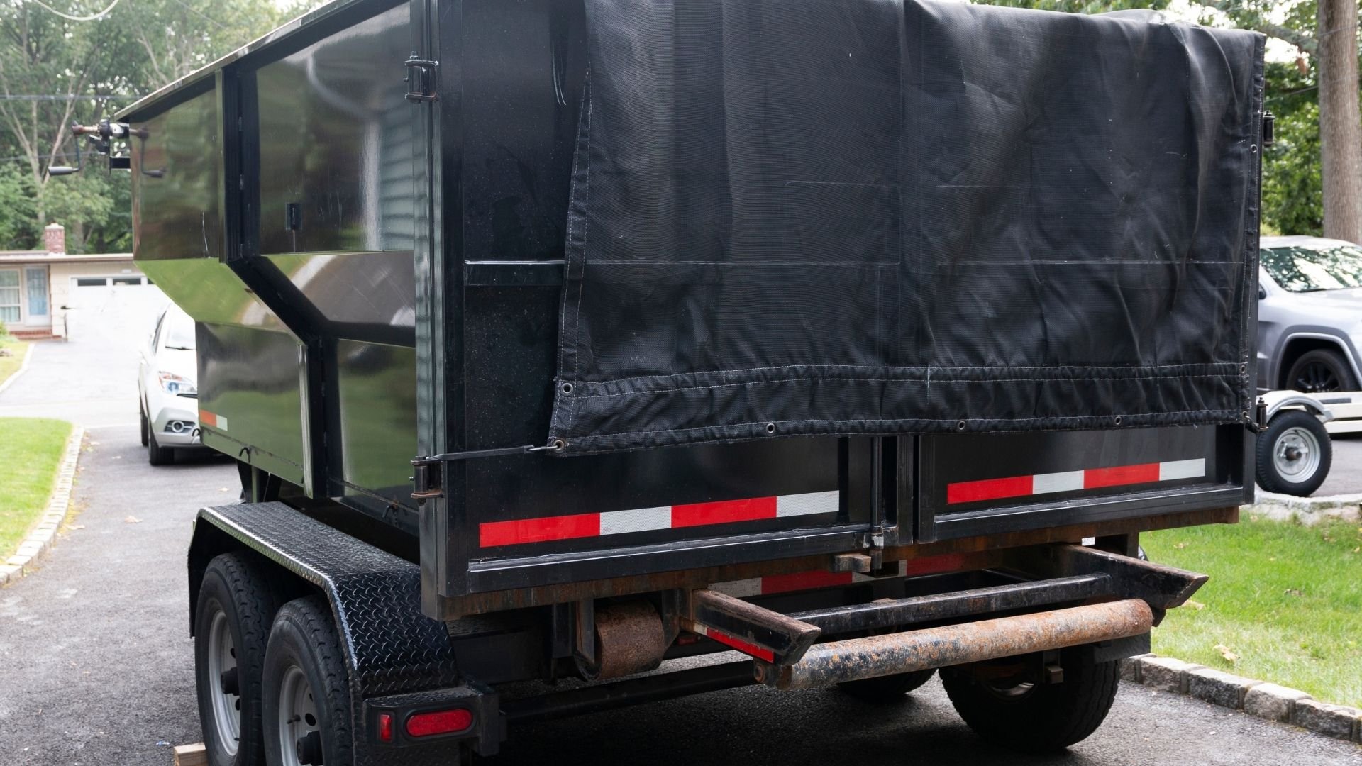 Black dump trailer with cover parked on residential street