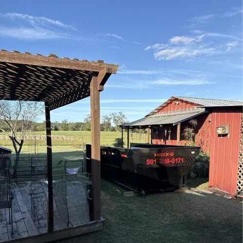 Red barn and wooden pergola with black dumpster on rural property