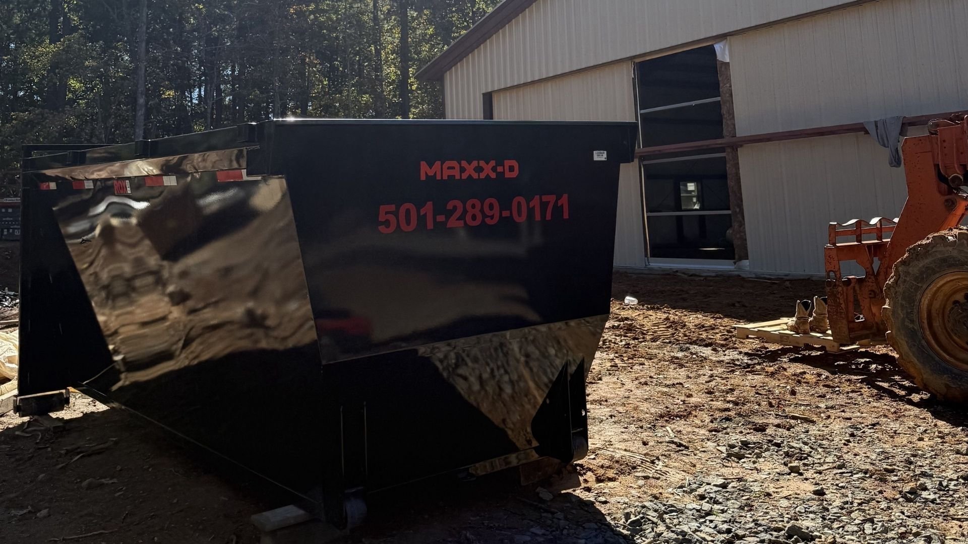 Black dumpster with Maxx-D logo at construction site near white building