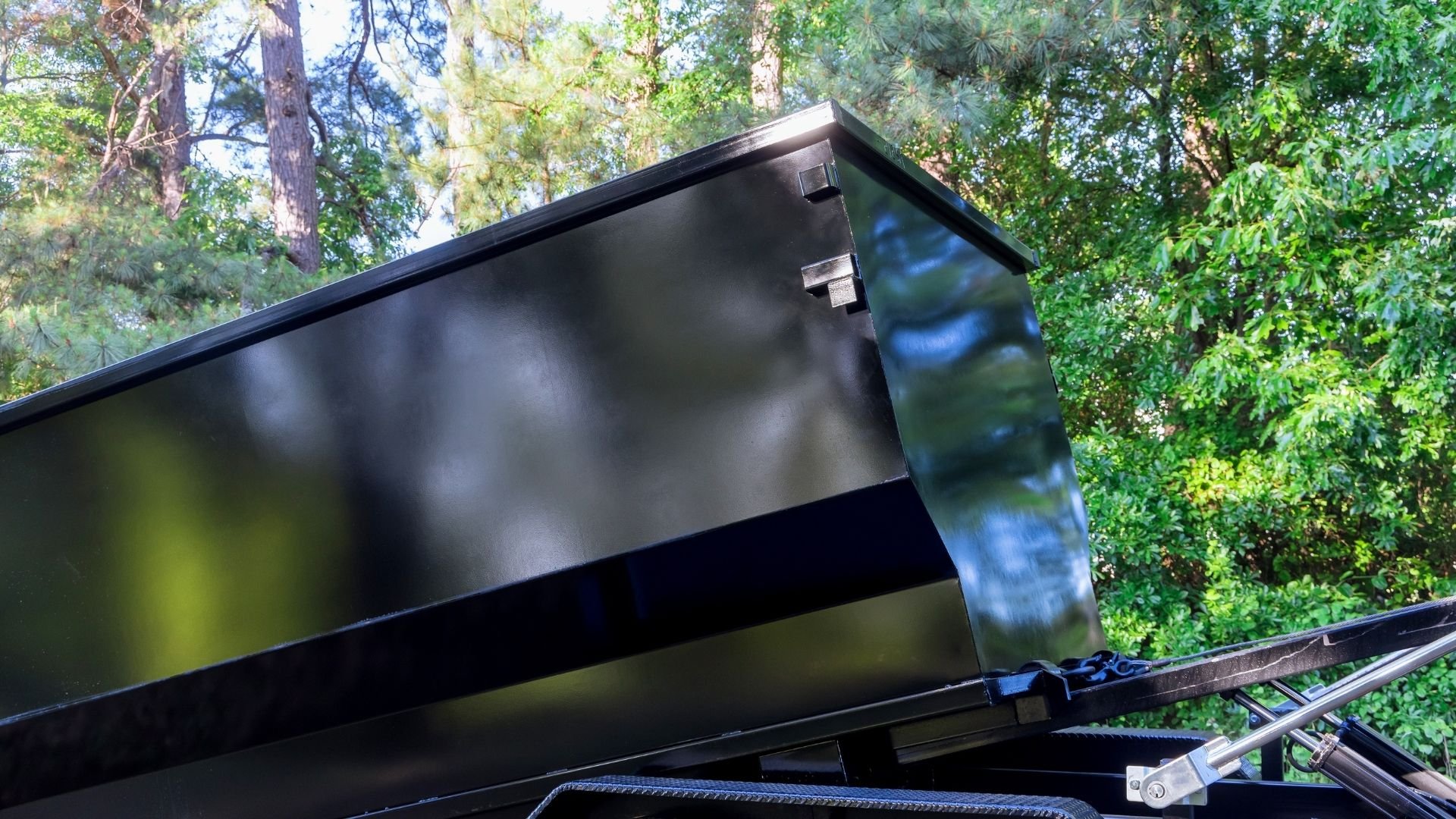 Black dumpster tilted open in a wooded forest area