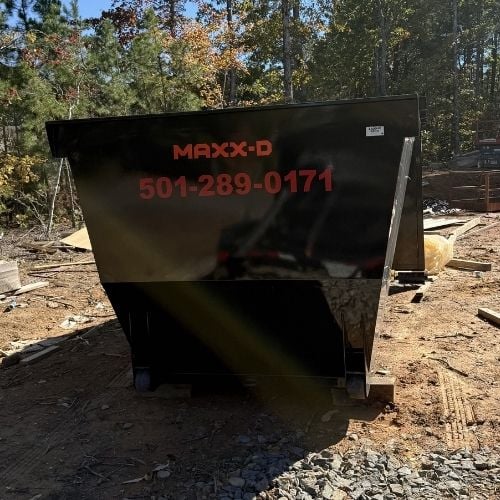 Large black dumpster with red logo on construction site with trees